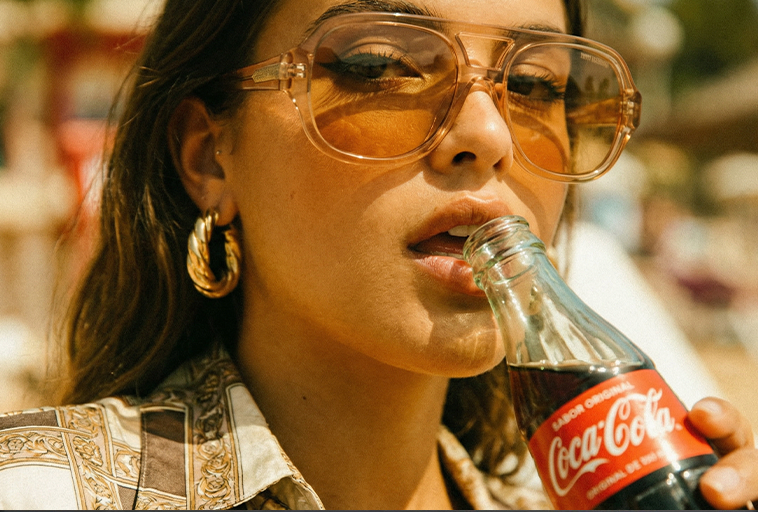 Retro lifestylebeeld van vrouw met gouden oorbellen en frisdrankfles