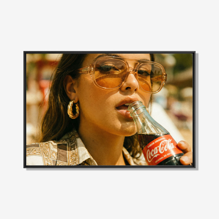 Vrouw met zonnebril drinkt uit Coca-Cola fles in warm zonlicht